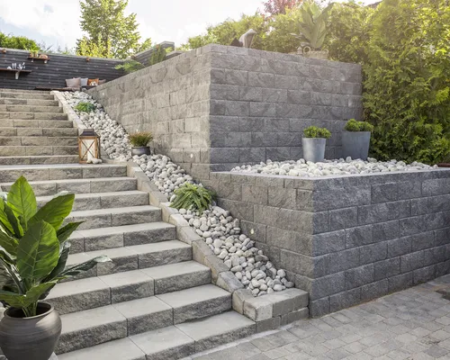 Stor Vertica støttemur i flere etasjer med belysning. Det er også en trapp hvor det er benyttet asak trappeelementer og elvestein som prikken over i-en